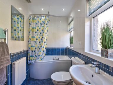 A bathroom with a bathtub shower combination with a pineapple patterned curtain a toilet a sink two windows with plants and blue tiles on the walls at Browside Little Arrow near Coniston