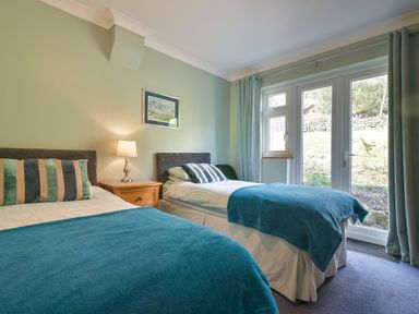 A bedroom with two single beds a nightstand with a lamp and a window with curtains at Browside Little Arrow near Coniston