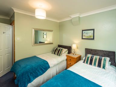 A bedroom with two single beds a wooden nightstand with a lamp and a mirror on the wall at Browside Little Arrow near Coniston