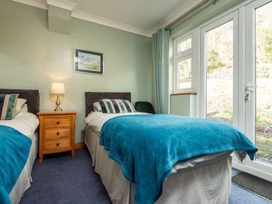 A bedroom with two single beds a wooden bedside table a lamp and glass doors at Browside in Little Arrow near Coniston