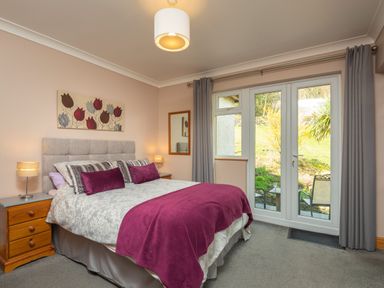 A bedroom with a bed two bedside tables lamps and glass doors leading outside at Browside Little Arrow near Coniston