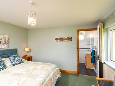 A bedroom with a bed a lamp a window an open door leading to a bathroom and a chair at Browside Little Arrow near Coniston