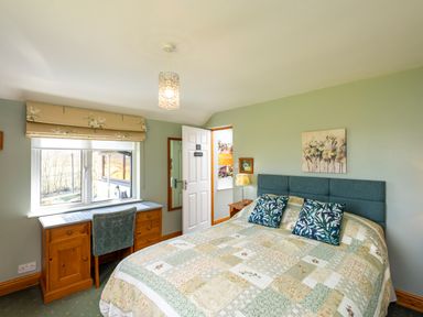 A bedroom with a double bed with patchwork quilt and pillows a wooden desk with a chair under a window and a door at Browside Little Arrow near Coniston