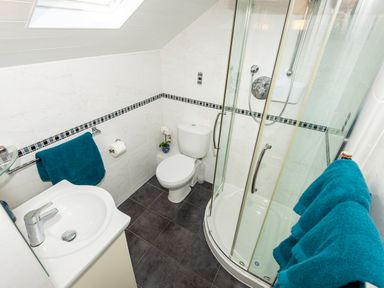 A bathroom with a sink, toilet, glass shower enclosure, and blue towels at Browside Little Arrow near Coniston