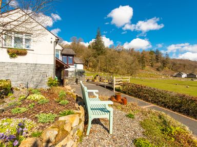 A garden bench and stone flower bed outside a house near a grassy field and trees at Browside Little Arrow near Coniston