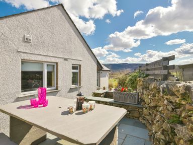 An outdoor patio area with a stone table and cups next to a stone wall and a house at Browside Little Arrow near Coniston