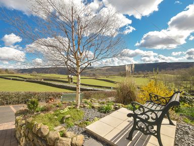 A garden with a bench a leafless tree and a stone wall overlooking green fields and hills at Browside in Little Arrow near Coniston