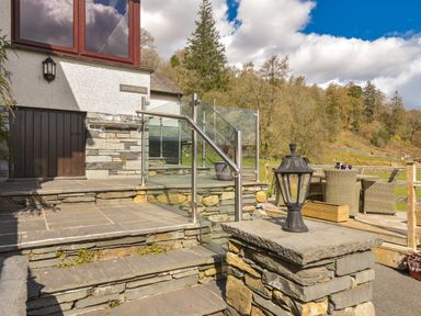 A stone staircase with metal and glass railing leading to a deck with outdoor furniture and a lamp post at Browside Little Arrow near Coniston