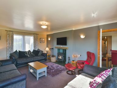 A living room with sofas a coffee table a television above a fireplace and a red armchair at Browside Little Arrow near Coniston
