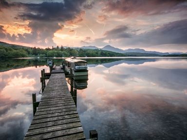 A wooden dock extending over a calm lake with a boat moored on the right side and mountains in the background at Browside in Little Arrow near Coniston