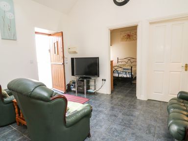 A living room with green leather chairs a wooden door a television and a view into a bedroom at Yr Hen Ysgubor in Trelech near St Clears