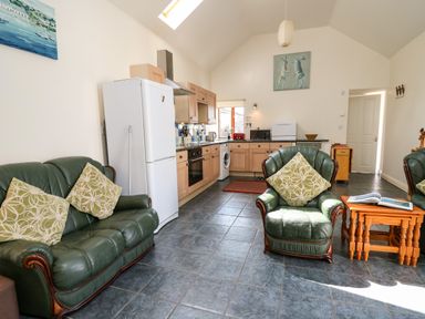 A living area with green leather sofas and a wooden table next to a kitchen with wooden cabinets and white appliances at Yr Hen Ysgubor Trelech near St Clears