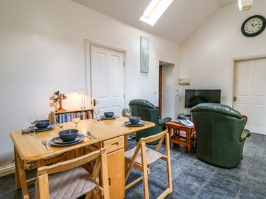 A dining table set with plates and glasses next to two green armchairs facing a television in a room at Yr Hen Ysgubor Trelech near St Clears