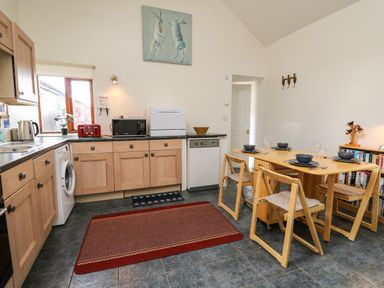 A kitchen with wooden cabinets a table set for four and kitchen appliances at Yr Hen Ysgubor in Trelech near St Clears