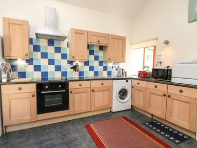 A kitchen with wooden cabinets a washing machine oven microwave toaster and a tiled backsplash at Yr Hen Ysgubor in Trelech near St Clears