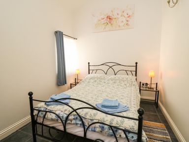 A bedroom with a metal bed frame blue curtains two bedside tables with lamps and a floral painting above the bed at Yr Hen Ysgubor Trelech near St Clears