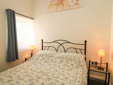 A bedroom with a bed with floral bedding two bedside tables with lamps and a window with curtains at Yr Hen Ysgubor in Trelech near St Clears