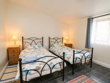A bedroom with two single beds with patterned bedding two wooden bedside tables with lamps and a window with curtains at Yr Hen Ysgubor in Trelech near St Clears