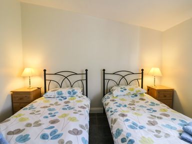 A bedroom with two single beds with floral bedding and wooden bedside tables with lamps at Yr Hen Ysgubor Trelech near St Clears