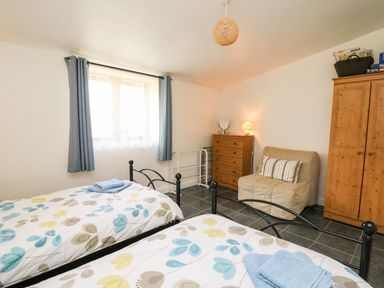A bedroom with two single beds a wooden chest of drawers a beige chair and a wooden wardrobe at Yr Hen Ysgubor in Trelech near St Clears