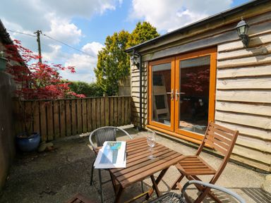 An outdoor patio with a wooden table and chairs next to a wooden building with glass double doors at Yr Hen Ysgubor in Trelech near St Clears