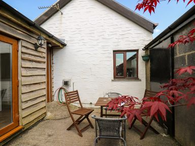 An outdoor patio with wooden chairs and a small table near a white building with a window at Yr Hen Ysgubor Trelech near St Clears