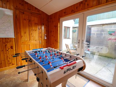 A foosball table in a wooden room with a door and glass patio doors showing an outdoor seating area at Yr Hen Ysgubor in Trelech near St Clears