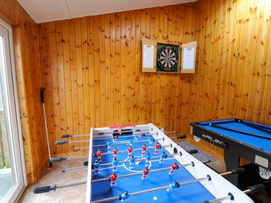 A game room with a foosball table a pool table and a dartboard on wood panel walls at Yr Hen Ysgubor in Trelech near St Clears