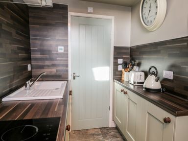 A kitchen with a sink stove kettle toaster knives and a clock on the wall at Nutshell in Whitby