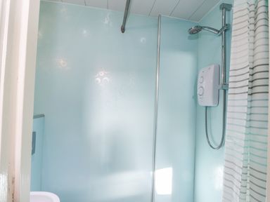 A bathroom with a showerhead water heater and striped shower curtain at Nutshell Whitby