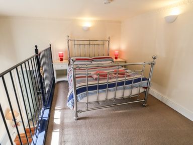 A bedroom with a metal bed frame striped bedding bedside tables with lamps and a black railing at Nutshell in Whitby