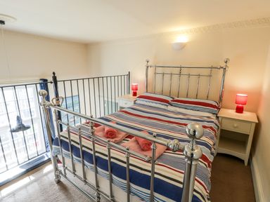A bedroom with a metal bed frame striped bedding two bedside tables with red lamps at Nutshell in Whitby
