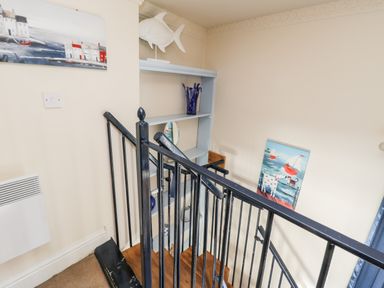A staircase with black metal railings next to a light blue shelving unit with decorative items and paintings on the walls at Nutshell in Whitby