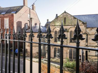 Black iron fence with pointed tops in front of stone buildings on a street at Nutshell in Whitby