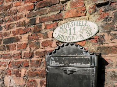A black metal mailbox attached to a brick wall with an oval white sign above it saying Nutshell 11 Brunswick St
