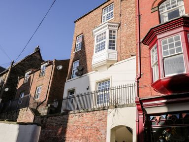 A row of brick buildings with bay windows and a staircase behind a black metal fence at Nutshell in Whitby