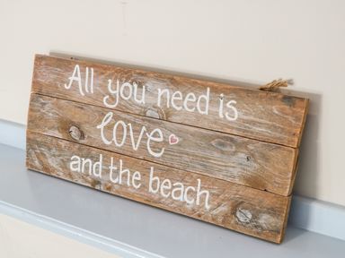 A wooden sign with the text All you need is love and the beach