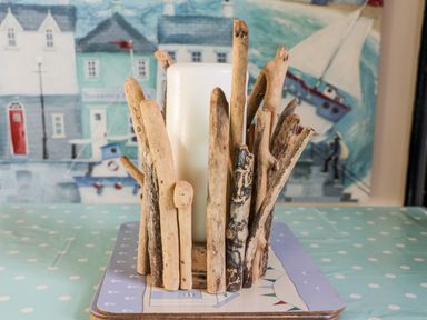 A white candle surrounded by upright driftwood sticks on a blue polka dot tablecloth with a nautical-themed background at Nutshell Whitby