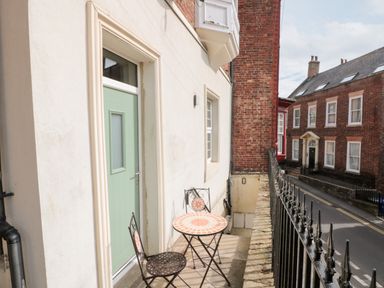 A small balcony with a round table and two chairs outside a green door overlooking a street with brick buildings at Nutshell in Whitby