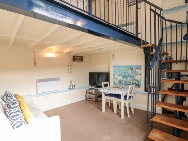A small living area with a sofa table and chairs a television and spiral staircase at Nutshell in Whitby