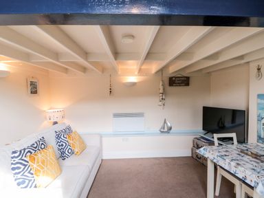 A living room with a sofa with yellow and blue cushions a television on a stand a table with a patterned cover and a small decorative sailboat on a shelf at Nutshell in Whitby