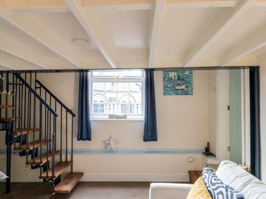 A living area with a spiral staircase window curtains cushions and a wall painting at Nutshell in Whitby