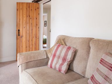 A beige sofa with patterned cushions beside a wooden door leading to a room with a bed at Crabtree in Hawkshead