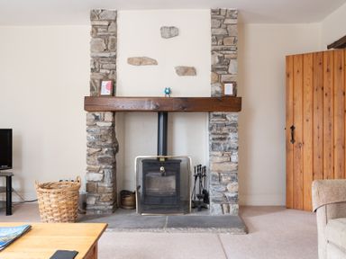 A living room with a stone fireplace wood burning stove and a wooden door at Crabtree in Hawkshead
