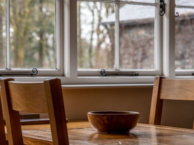 A wooden table with a wooden bowl and wooden chairs near a window at Crabtree in Hawkshead
