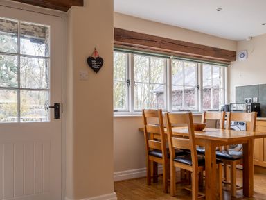 A kitchen dining area with a wooden table and chairs near large windows and a door at Crabtree in Hawkshead