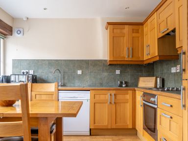 A kitchen with wooden cabinets a dining table chairs a dishwasher oven and countertop appliances at Crabtree in Hawkshead