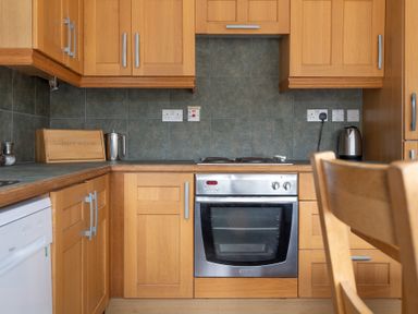 A kitchen with wooden cabinets a stovetop an oven and a kettle at Crabtree in Hawkshead