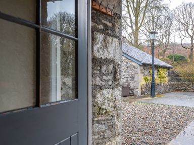 A stone wall with a window next to a gravel driveway and a street lamp at Crabtree in Hawkshead
