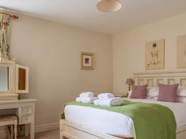 A bedroom with a white wooden bed with green blanket and rolled white towels and a vanity with mirror at Crabtree in Hawkshead